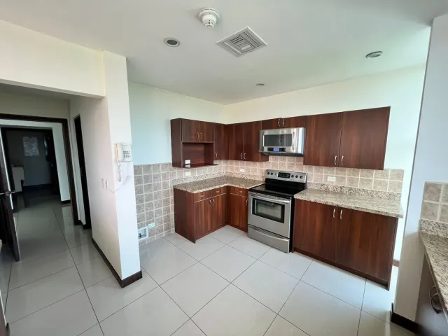 Kitchen corner with dark wooden cabinets, granite countertops, and stainless steel appliances, plus light-colored floor tiles.