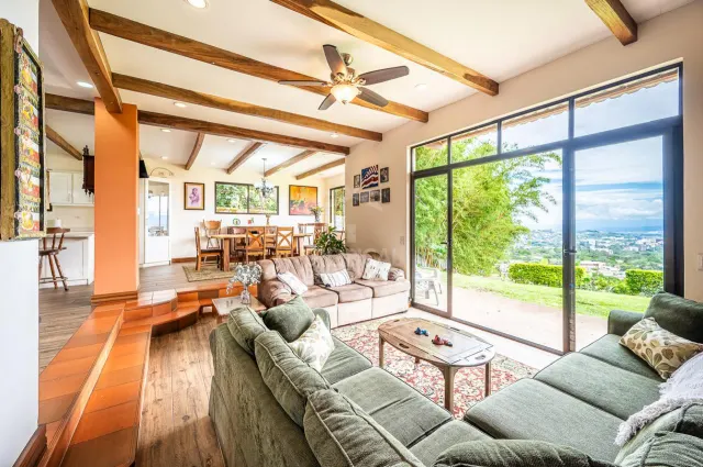 Living area with green sofa and coffee table next to large glass doors showing a grassy landscape. Steps lead up to a dining space with a wooden table and chairs.