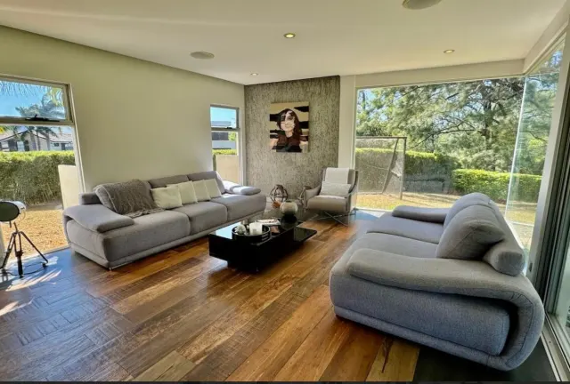 Living area with two gray fabric sofas, a black coffee table, wood-plank flooring, and large windows looking out to greenery.