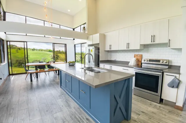 Kitchen featuring a blue center island, stainless steel appliances, white cabinets, and large windows looking out to green hills.
