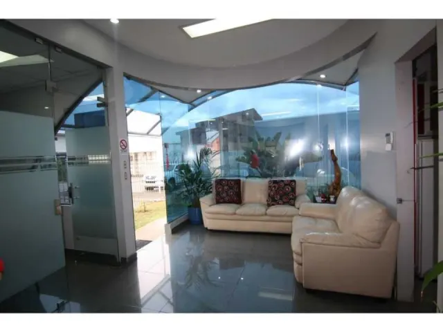 Reception room with glossy tile floors, a curved glass wall overlooking the exterior, and two white leather sofas.