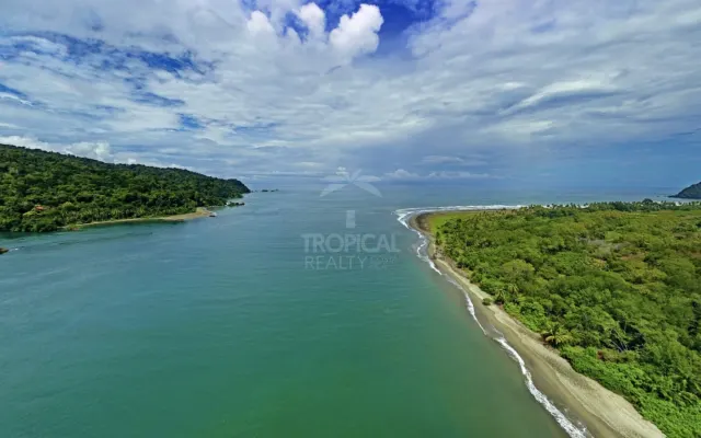 Aerial view of a coastal inlet with forested land bordering the water and beach under a cloudy sky.