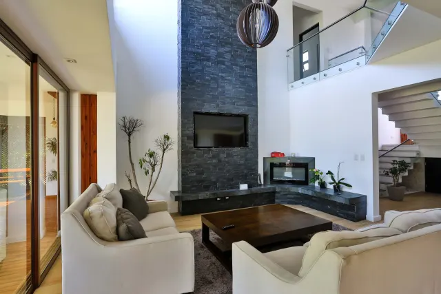 Living room featuring a tall dark stone accent wall with a mounted television, a central dark wood coffee table, and two white sofas.