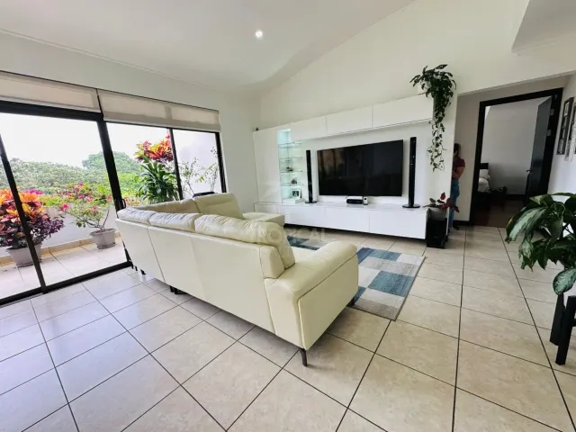 Living room featuring a light-colored leather sofa, a large wall-mounted television unit, and sliding glass doors leading to a balcony.