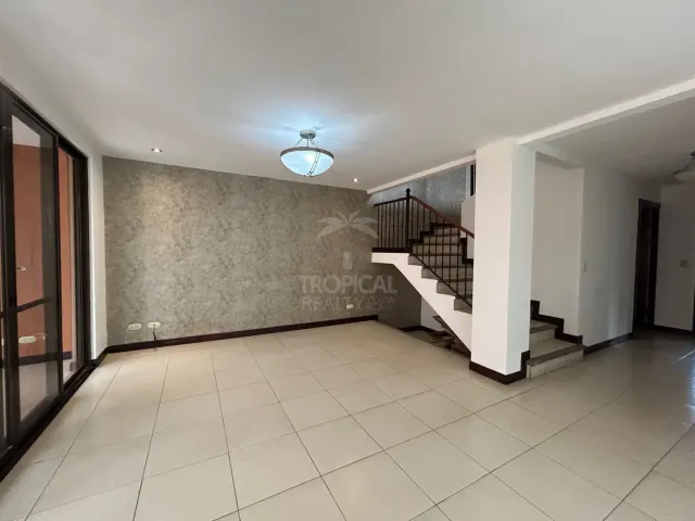 An empty living room with light tile flooring, a grey textured accent wall, and a staircase with metal railings leading upstairs.