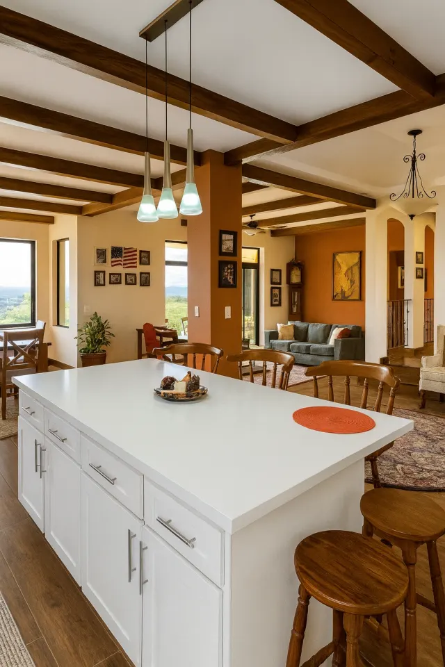 Kitchen island featuring white cabinets and a white countertop, with three pendant lights overhead and dark wood ceiling beams throughout.