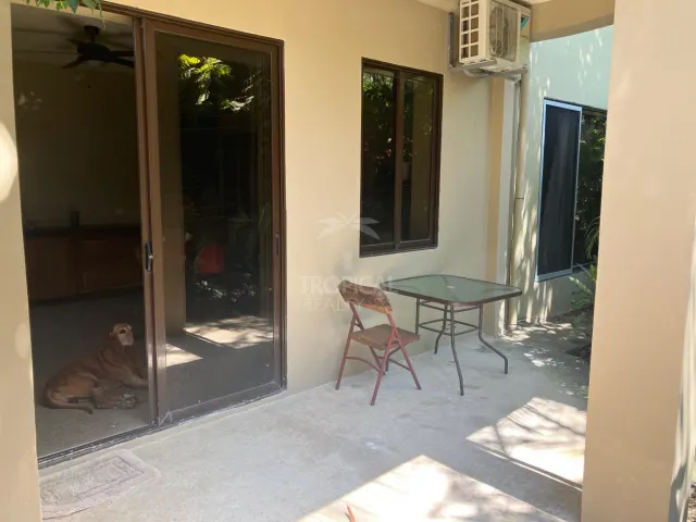 Covered concrete patio with a glass-topped table, a metal chair, and sliding glass doors leading indoors.
