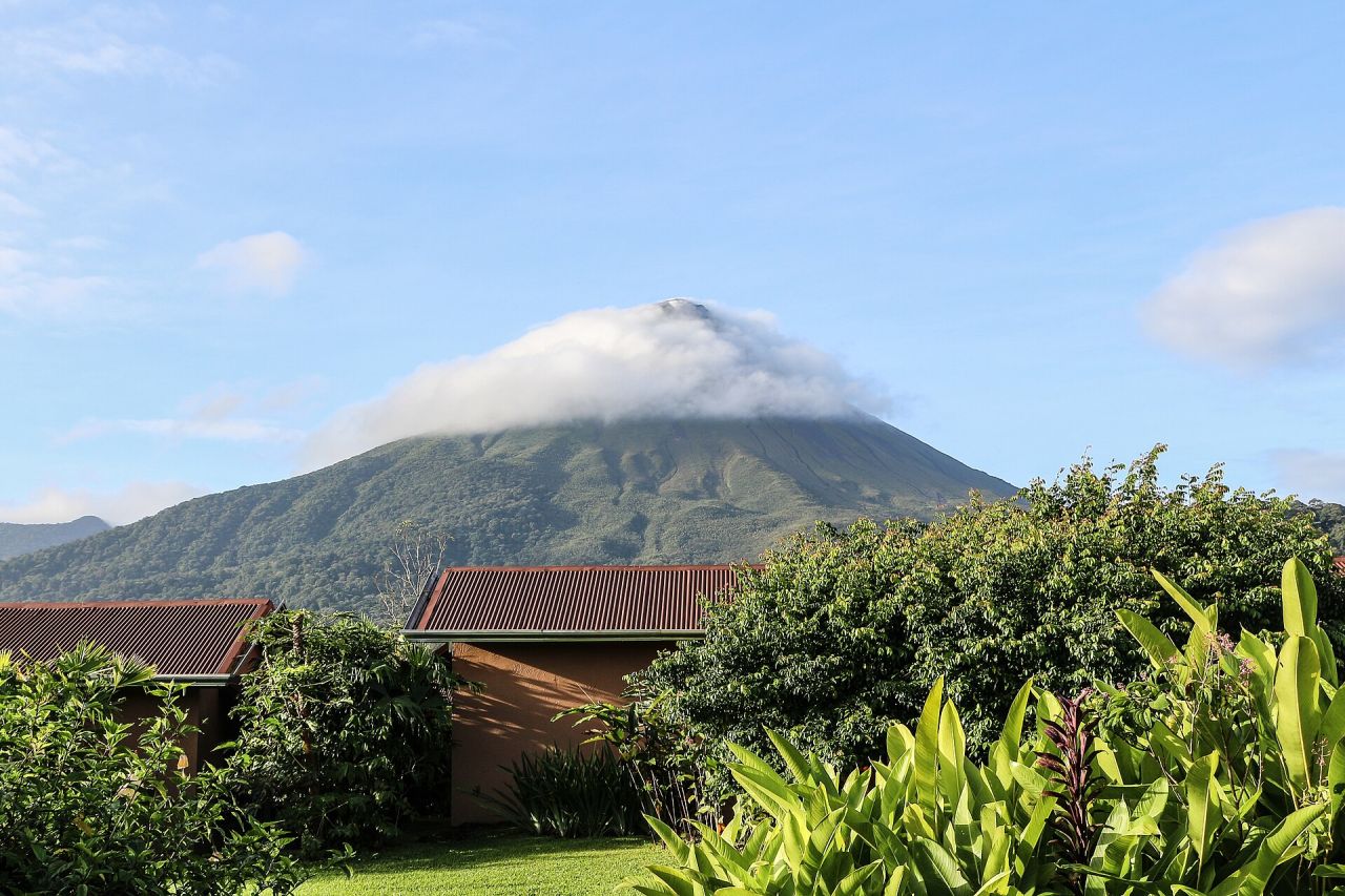 Arenal volcano wearing a collar of cloud, seen over the rooftops and gardens of La Fortuna